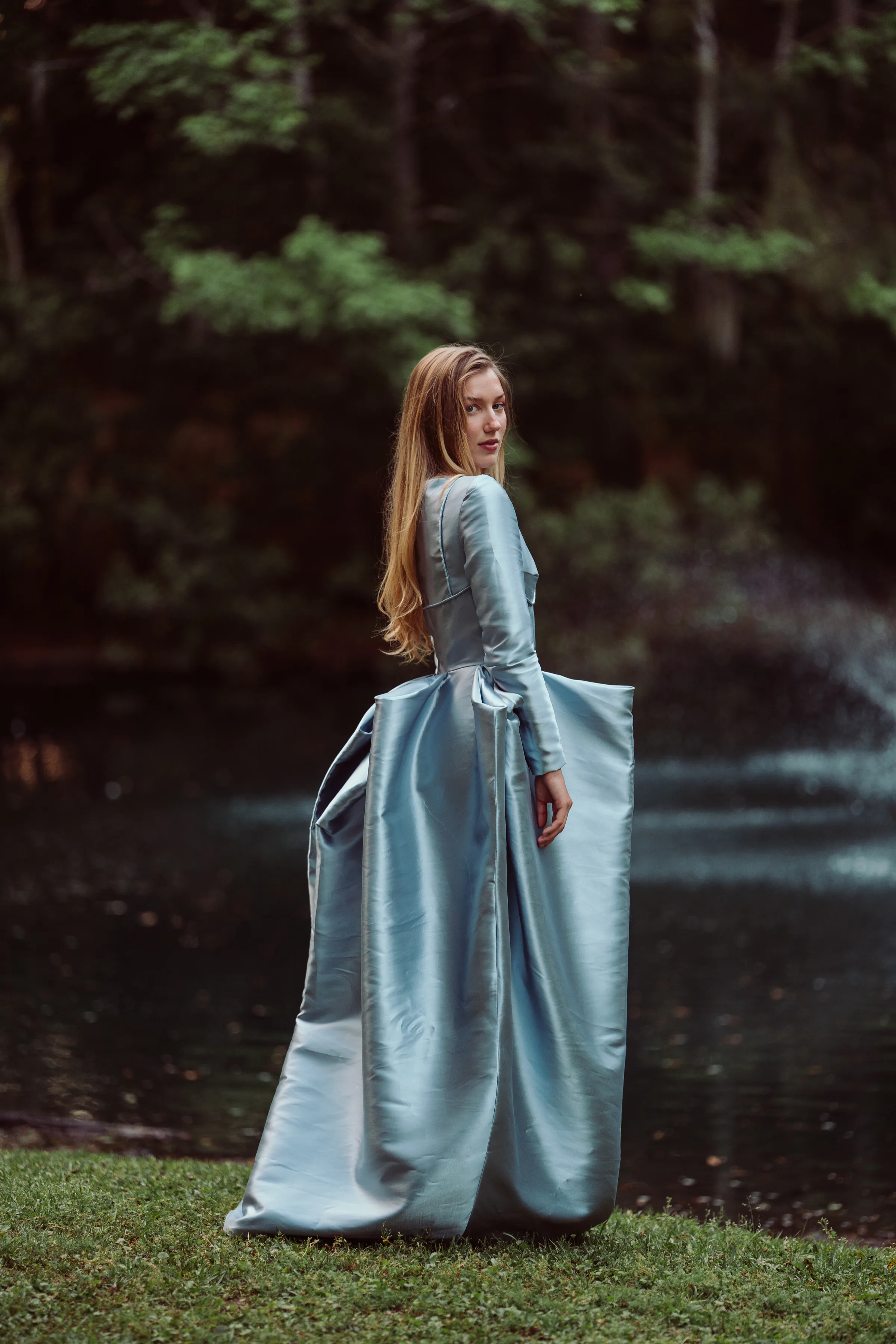 Model wearing Isolde, a silver-blue satin evening gown with long sleeves and an architectural pannier skirt