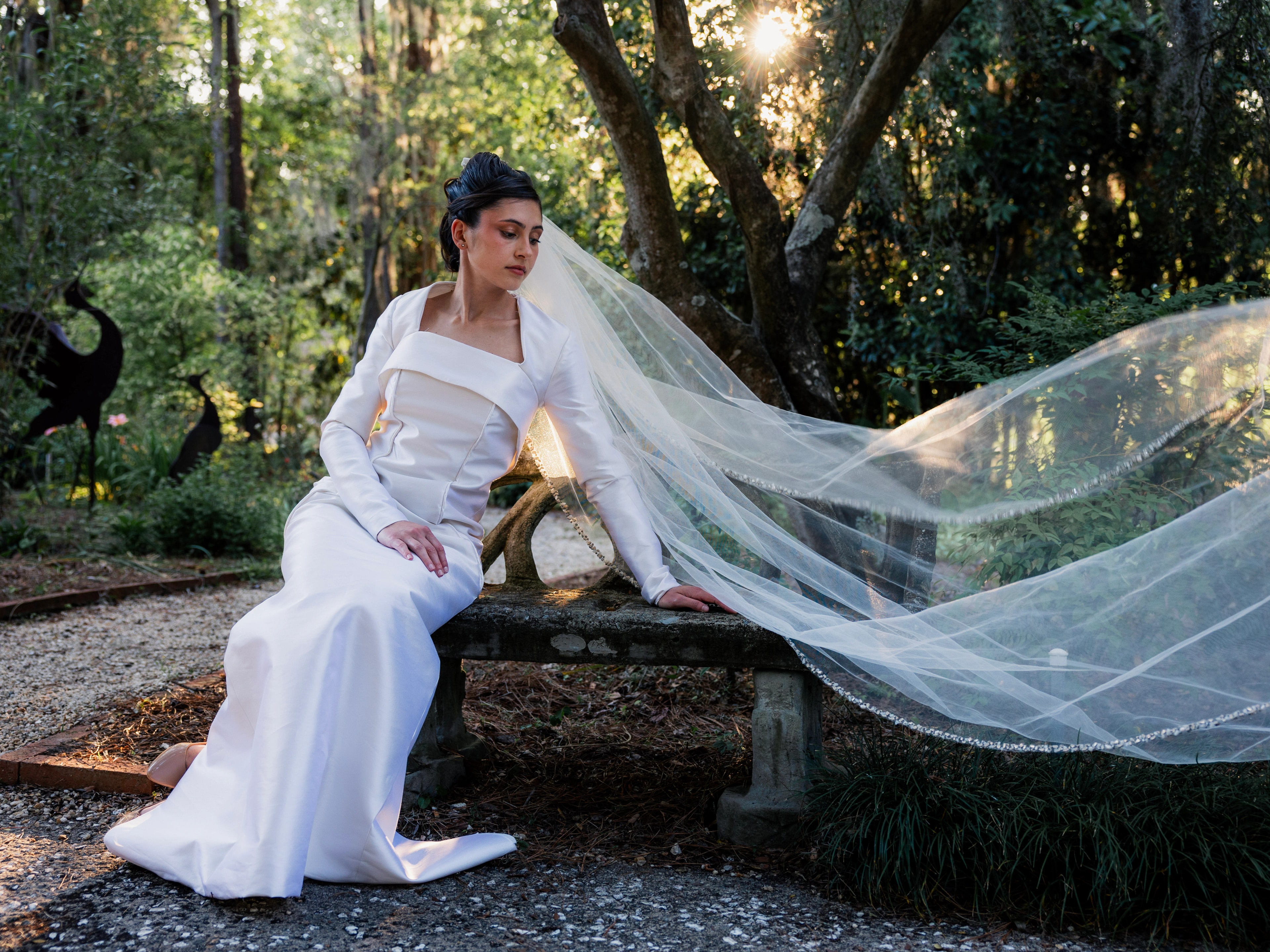 Bride seated in Niah wedding gown with a jeweled-edge veil flowing through the garden