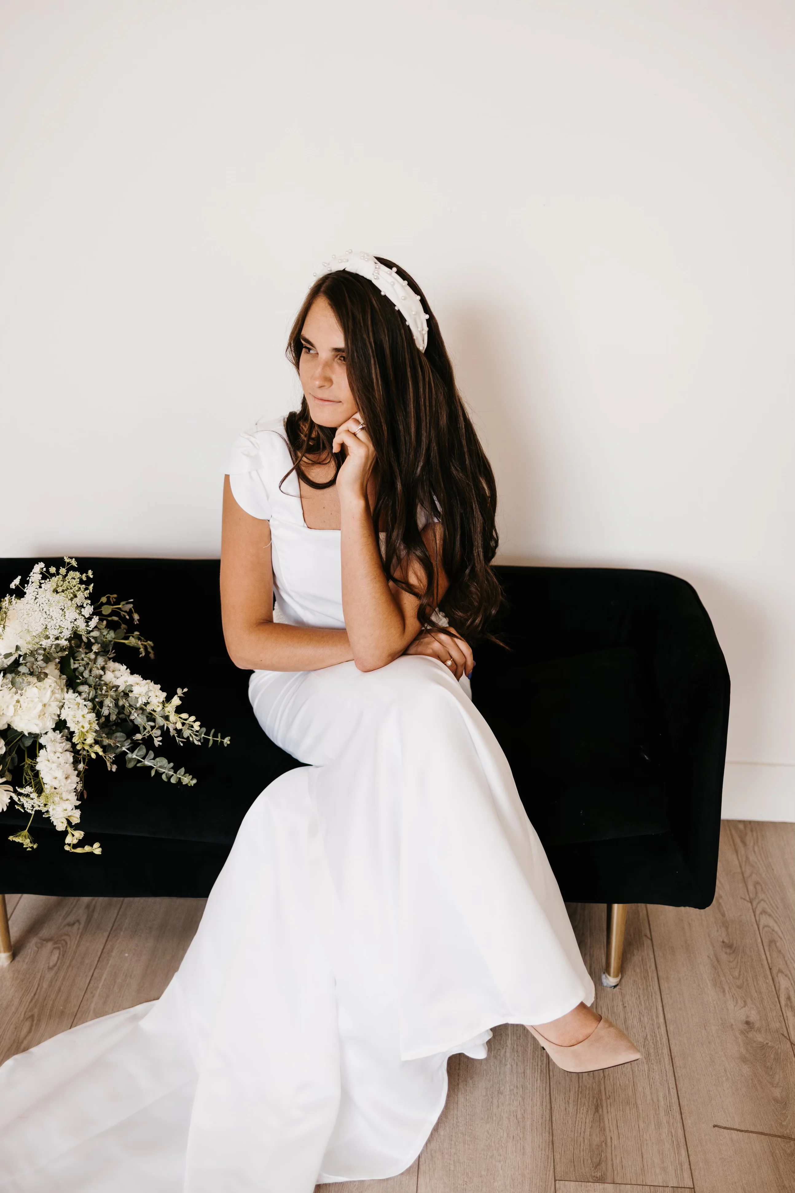 A closer seated portrait of the first wedding dress styled with a pearl headband and white bouquet.