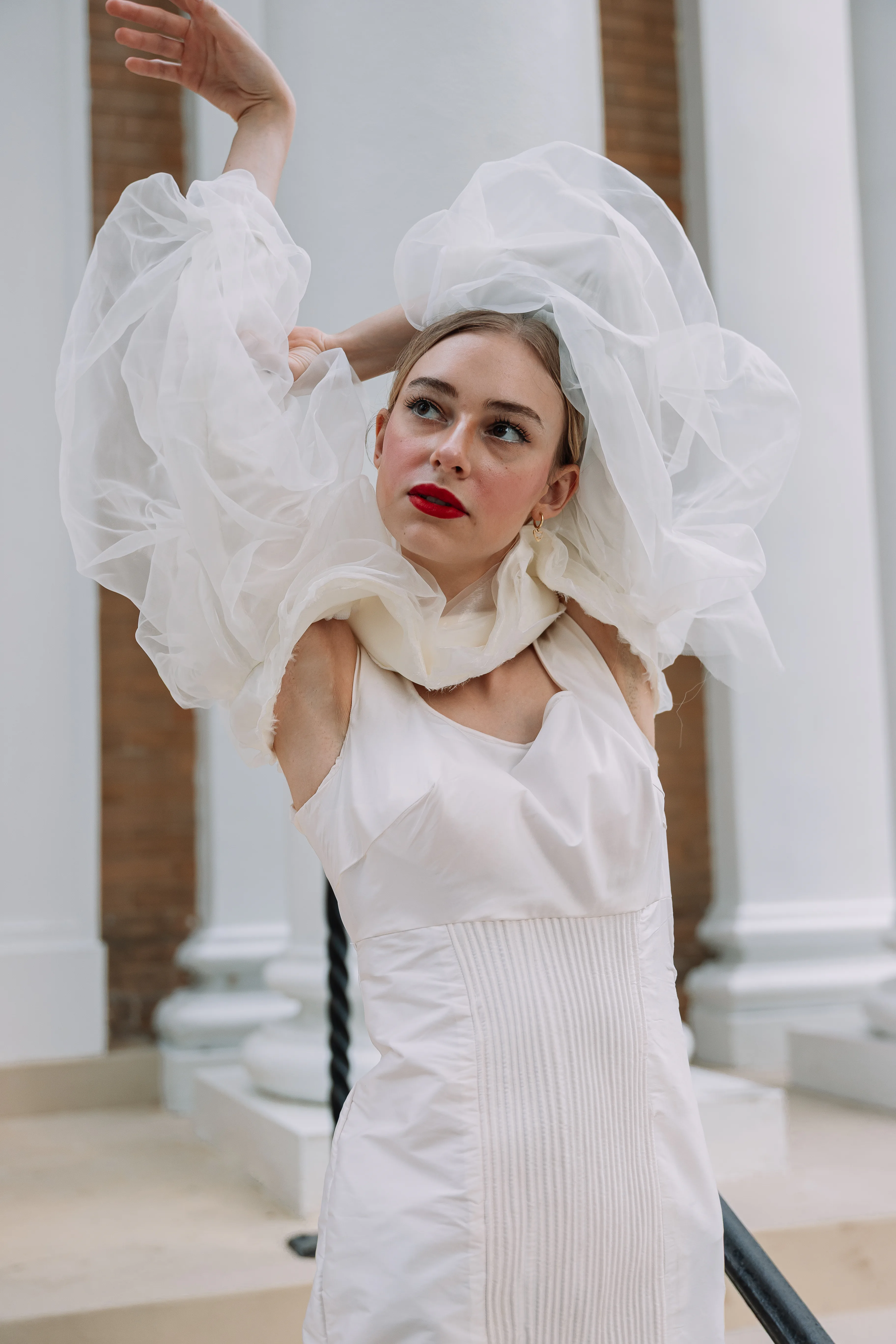 A portrait of the white conceptual garment with translucent organza sleeve volume framing the model's face and shoulders.