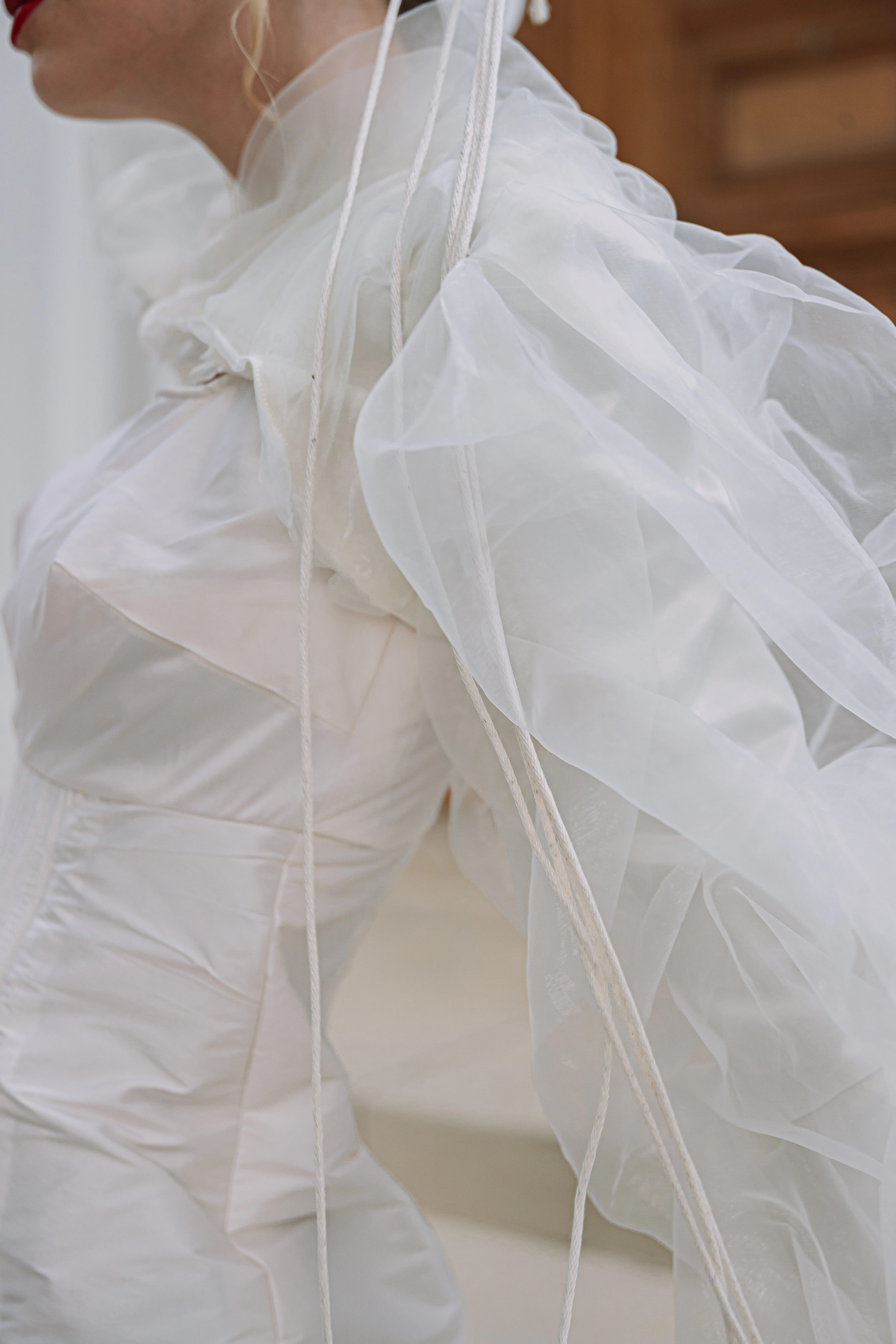 A close side detail of translucent white sleeve layers, cord accents, and sculpted bodice seams.