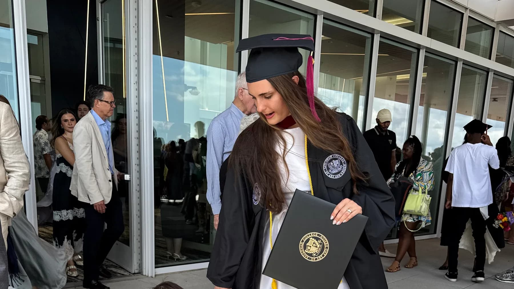 Samantha Covey in her SCAD graduation regalia holding her diploma beside a young child.