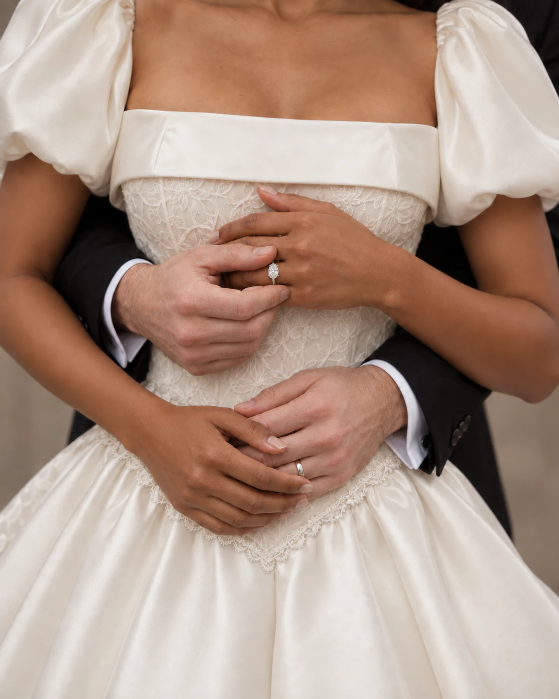 Close view of Cecilia's floral lace bodice, folded satin neckline, and pointed waist with the couple's hands resting together