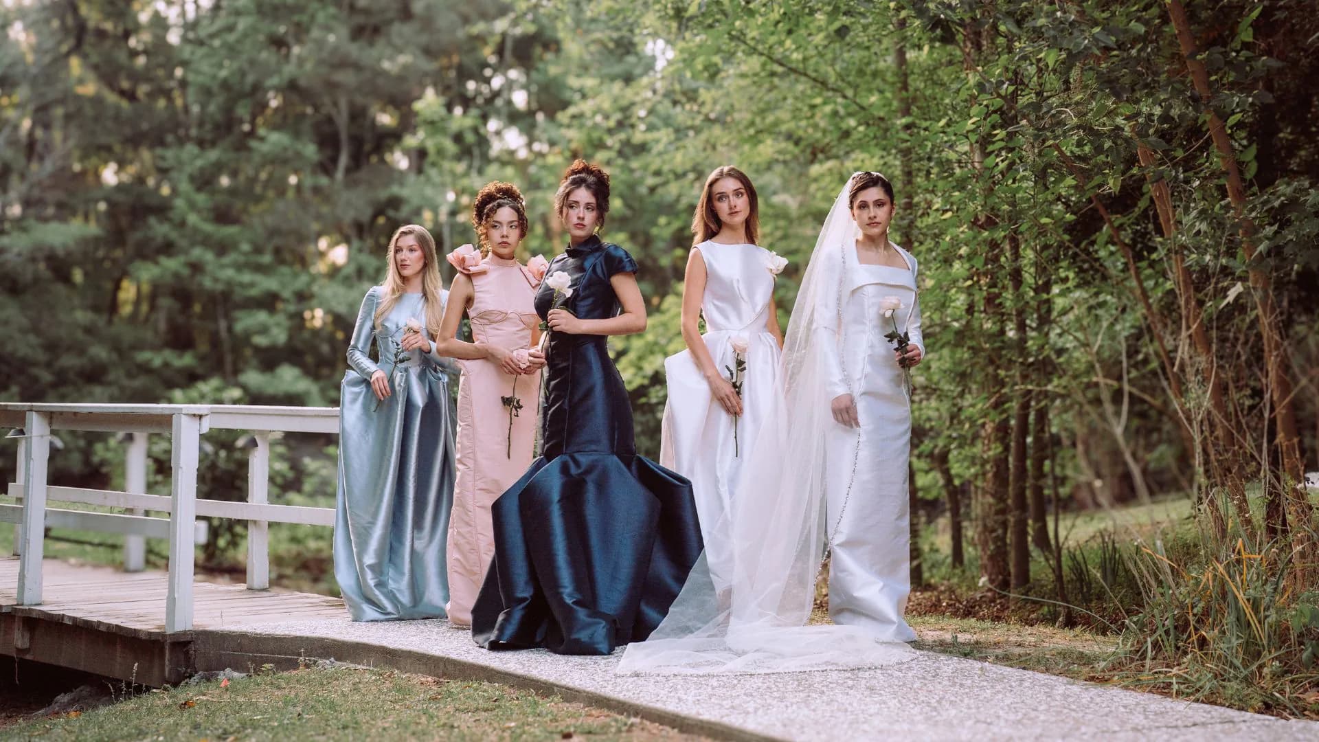 Five women from the Because She Is a Mother collection posed together at the edge of a white garden bridge.