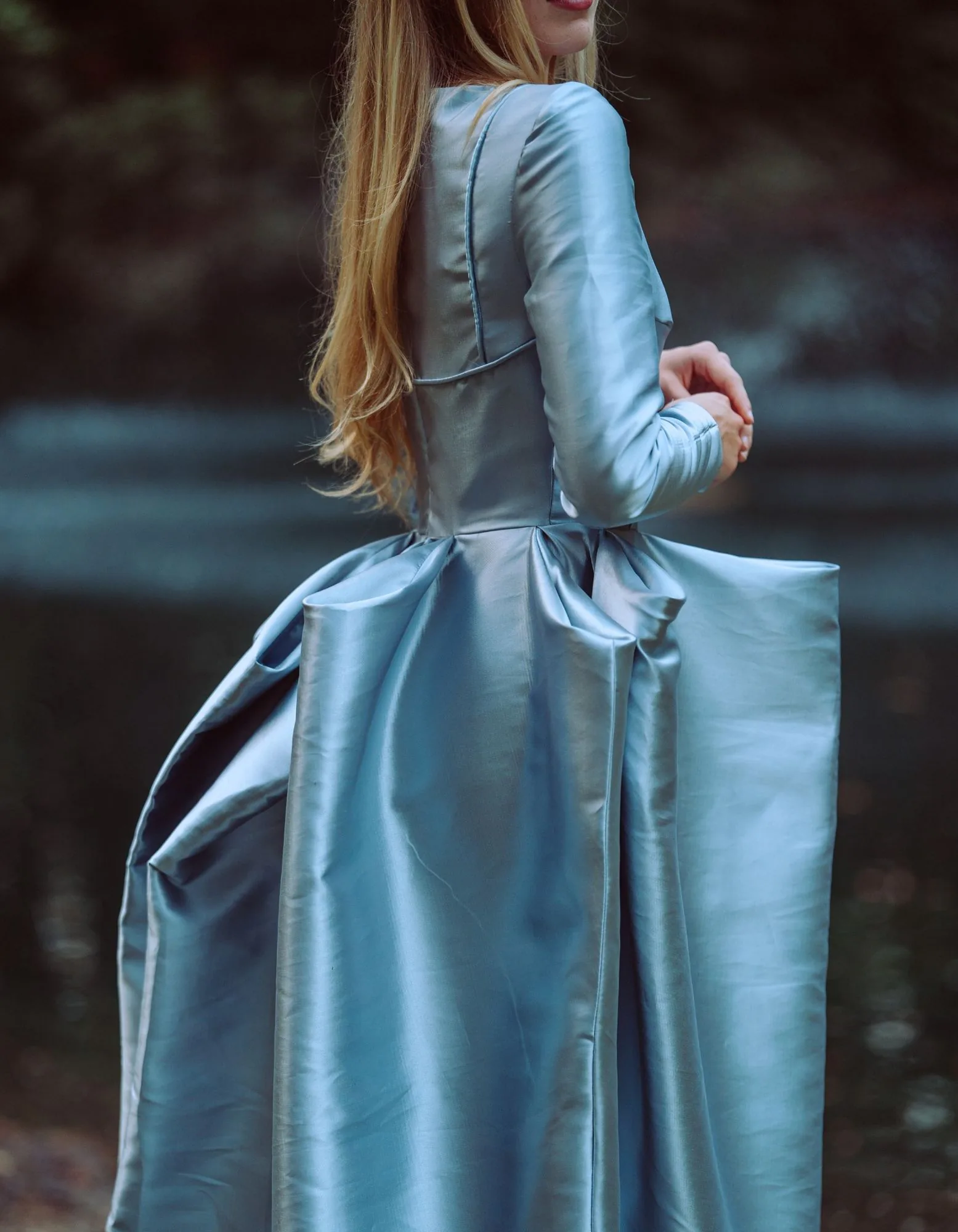 The back bow volume of a powder-blue gown beside the water.