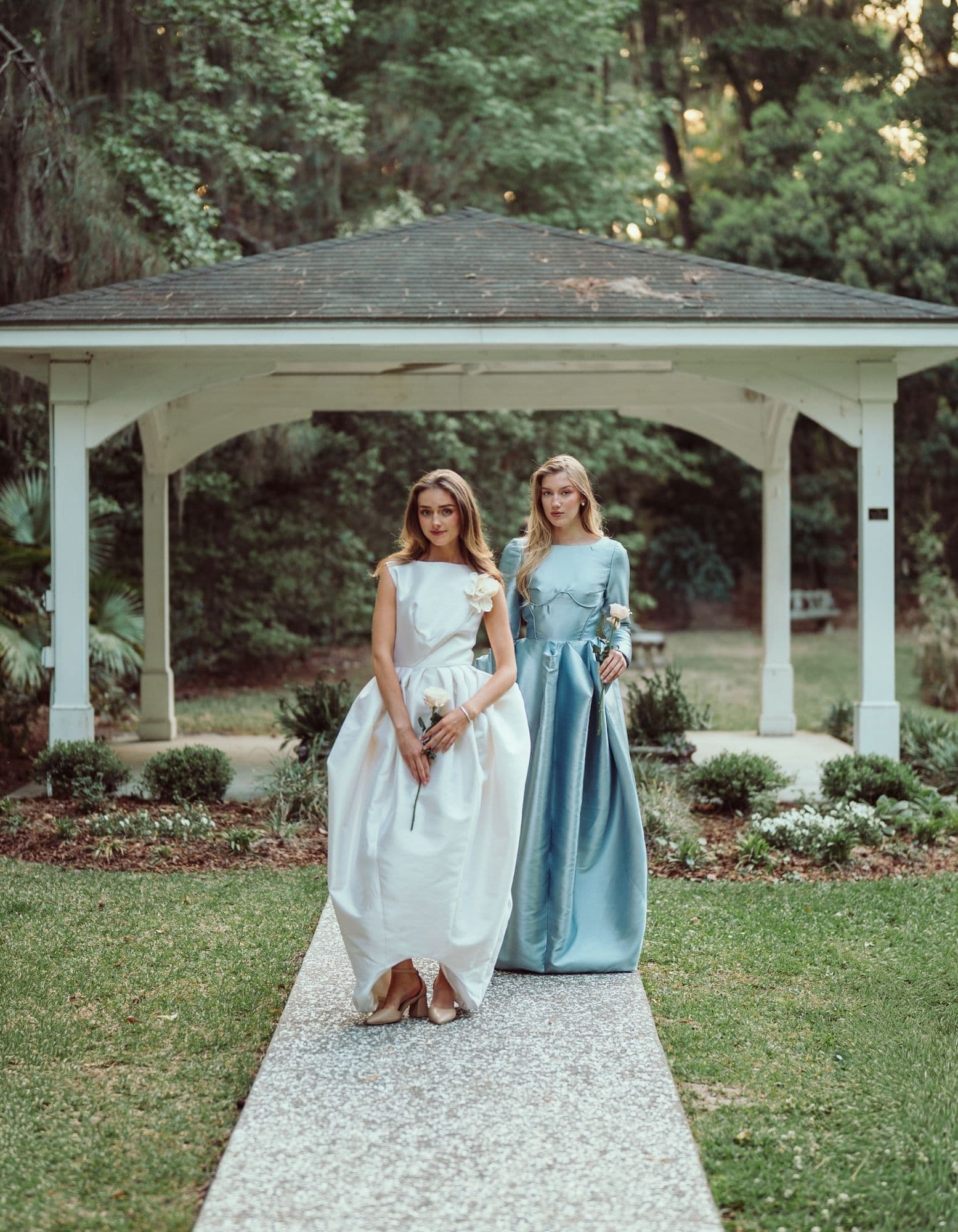 Two gowns posed beneath a white gazebo in the garden.