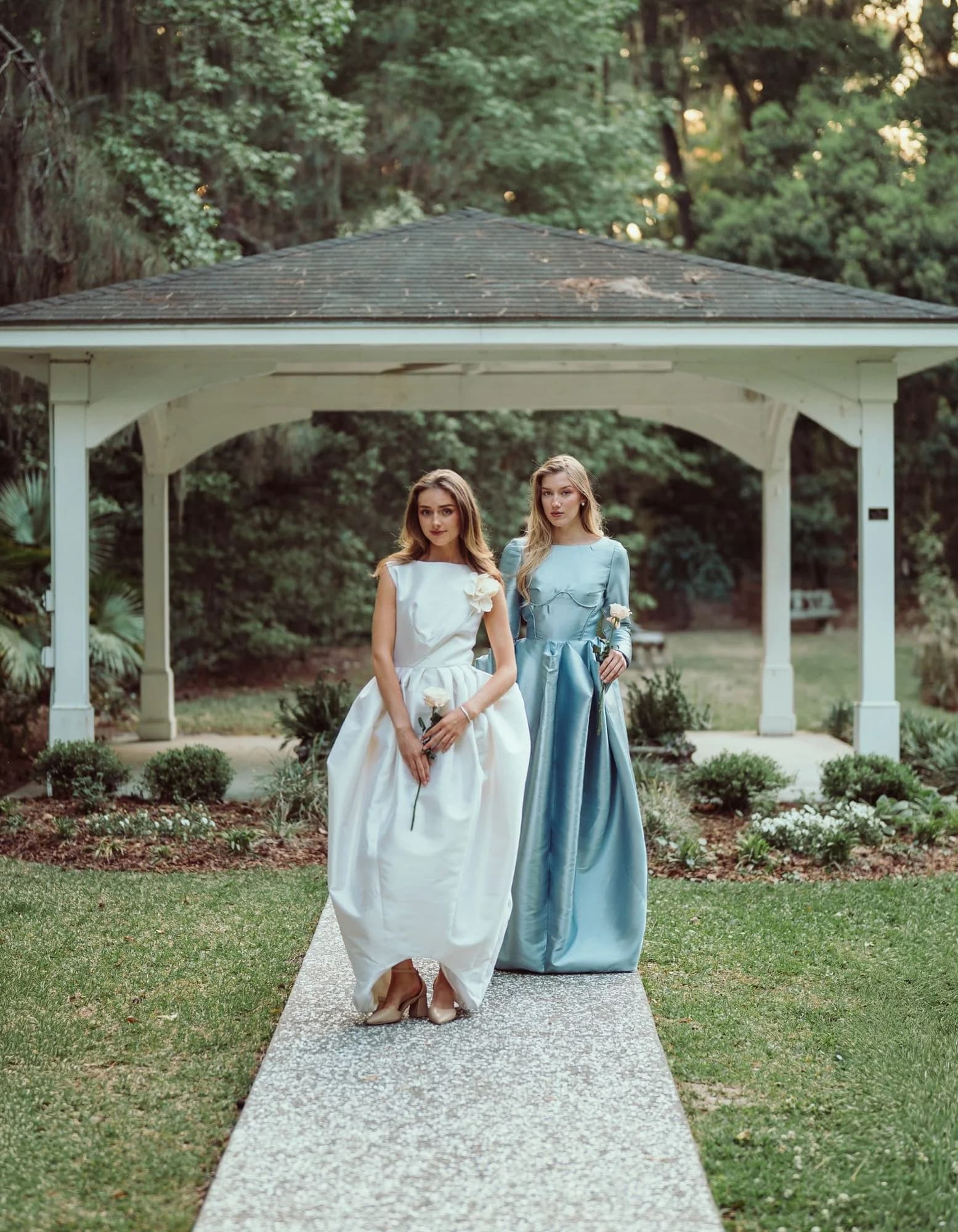 Two gowns posed beneath a white gazebo in the garden.
