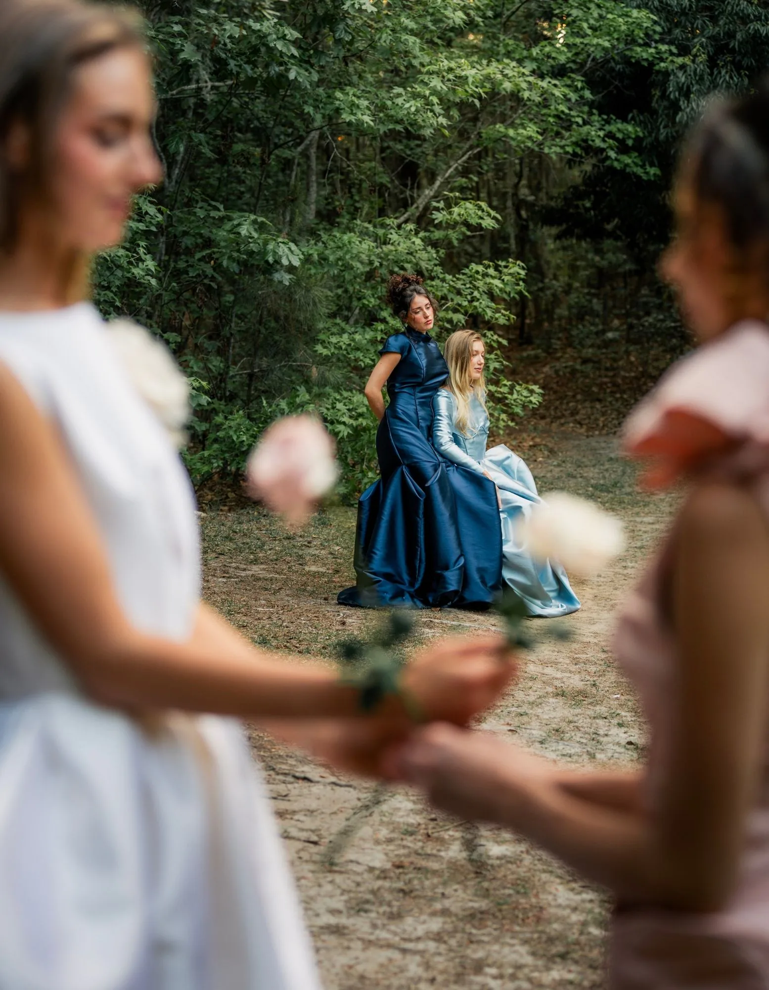 Two evening gowns framed in the distance between softly blurred foreground figures.