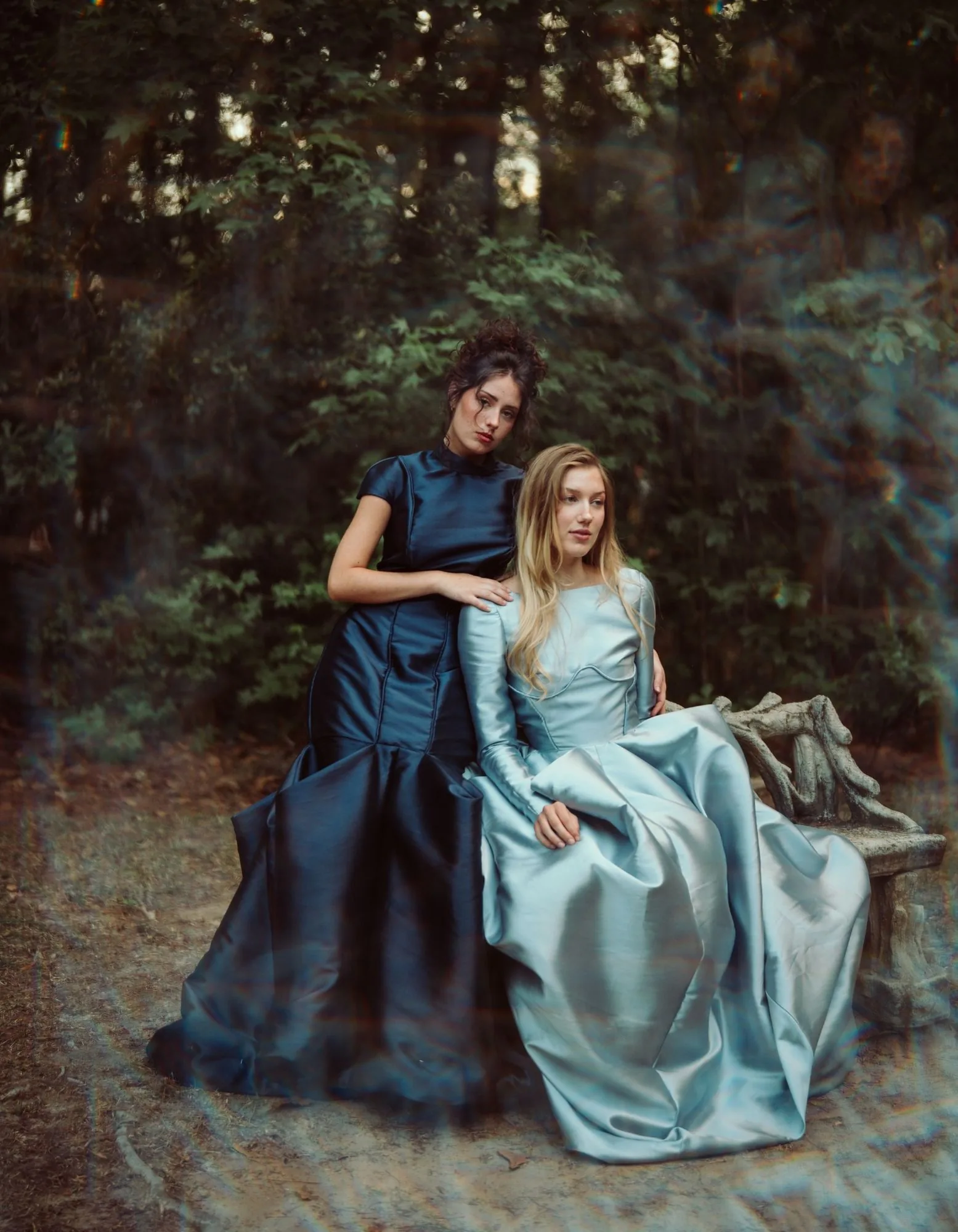 A navy gown and powder-blue gown styled together on a stone bench in the woods.
