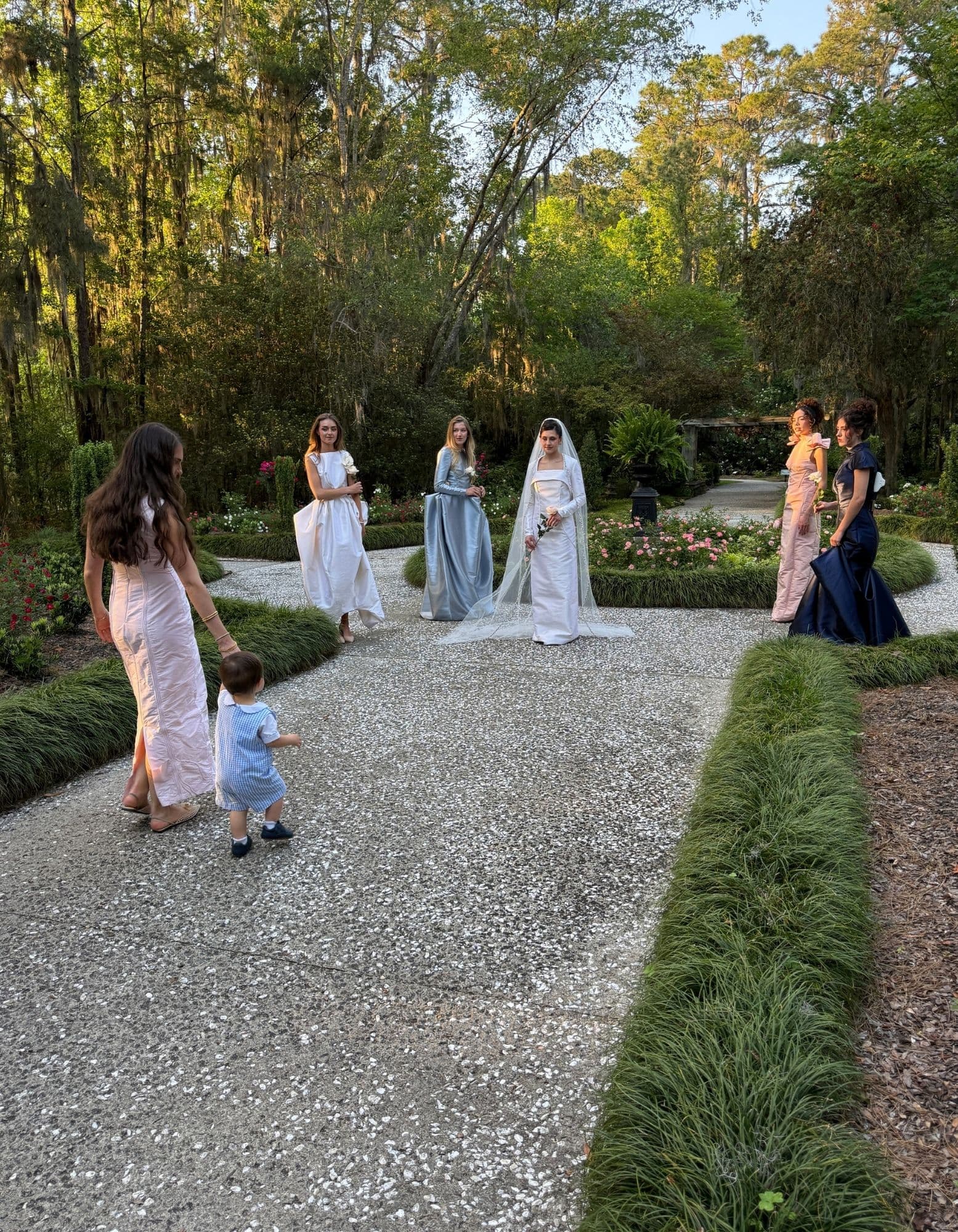 Models gathering on a garden path while the Because She Is a Mother shoot is arranged around them.