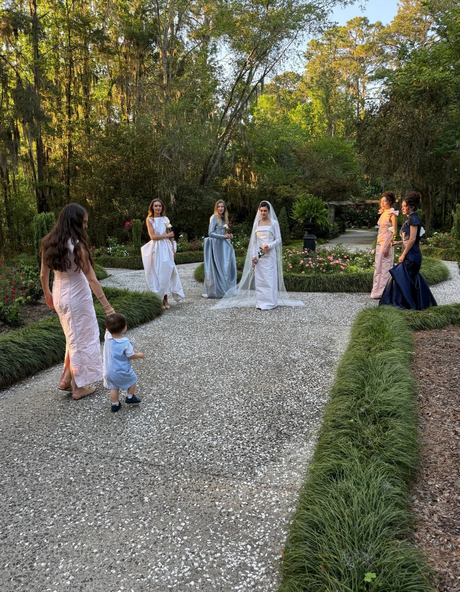 Models gathering on a garden path while the Because She Is a Mother shoot is arranged around them.