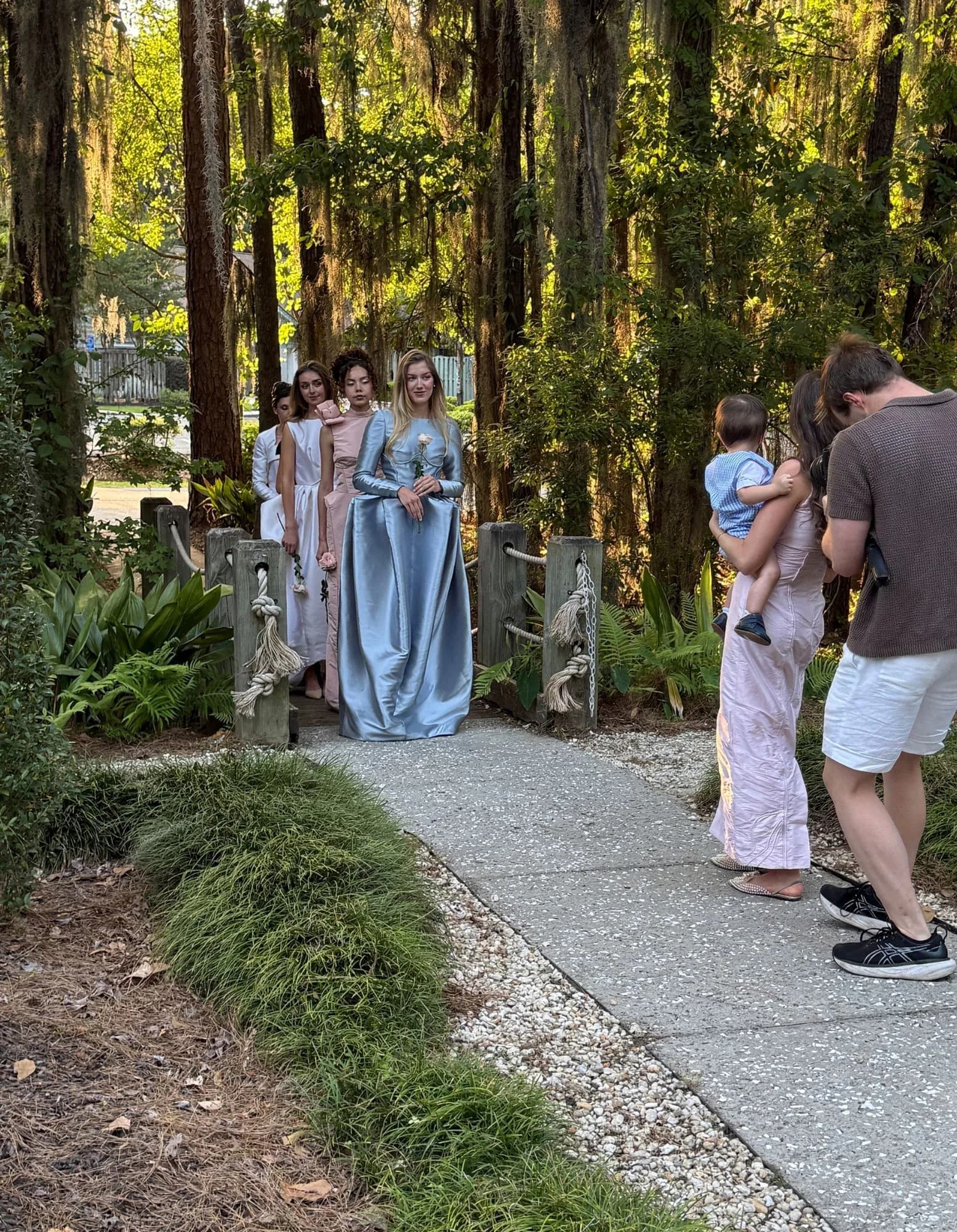 A behind-the-scenes garden procession with models waiting on a wooded path during the shoot.