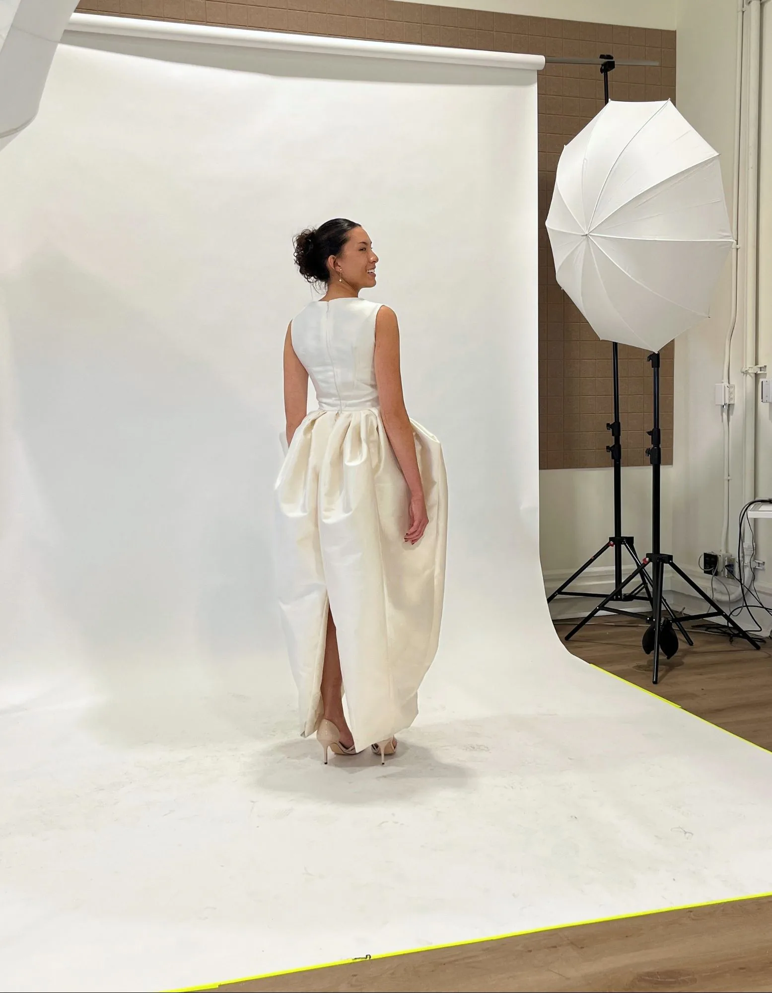 A model turning on a studio backdrop to show the back of an ivory gown during fittings and photography.