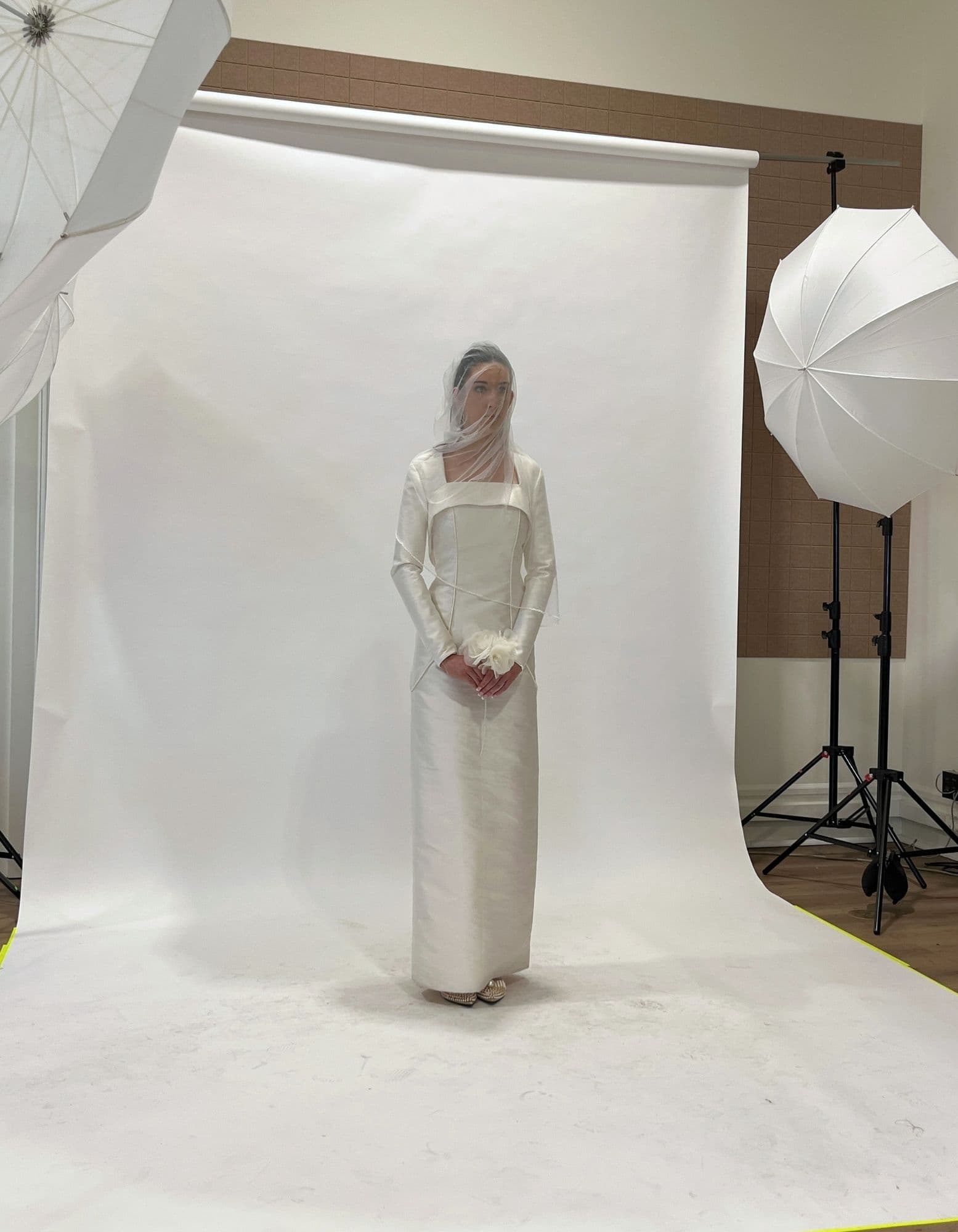 A veiled bridal look photographed in studio between white umbrellas and a paper backdrop.