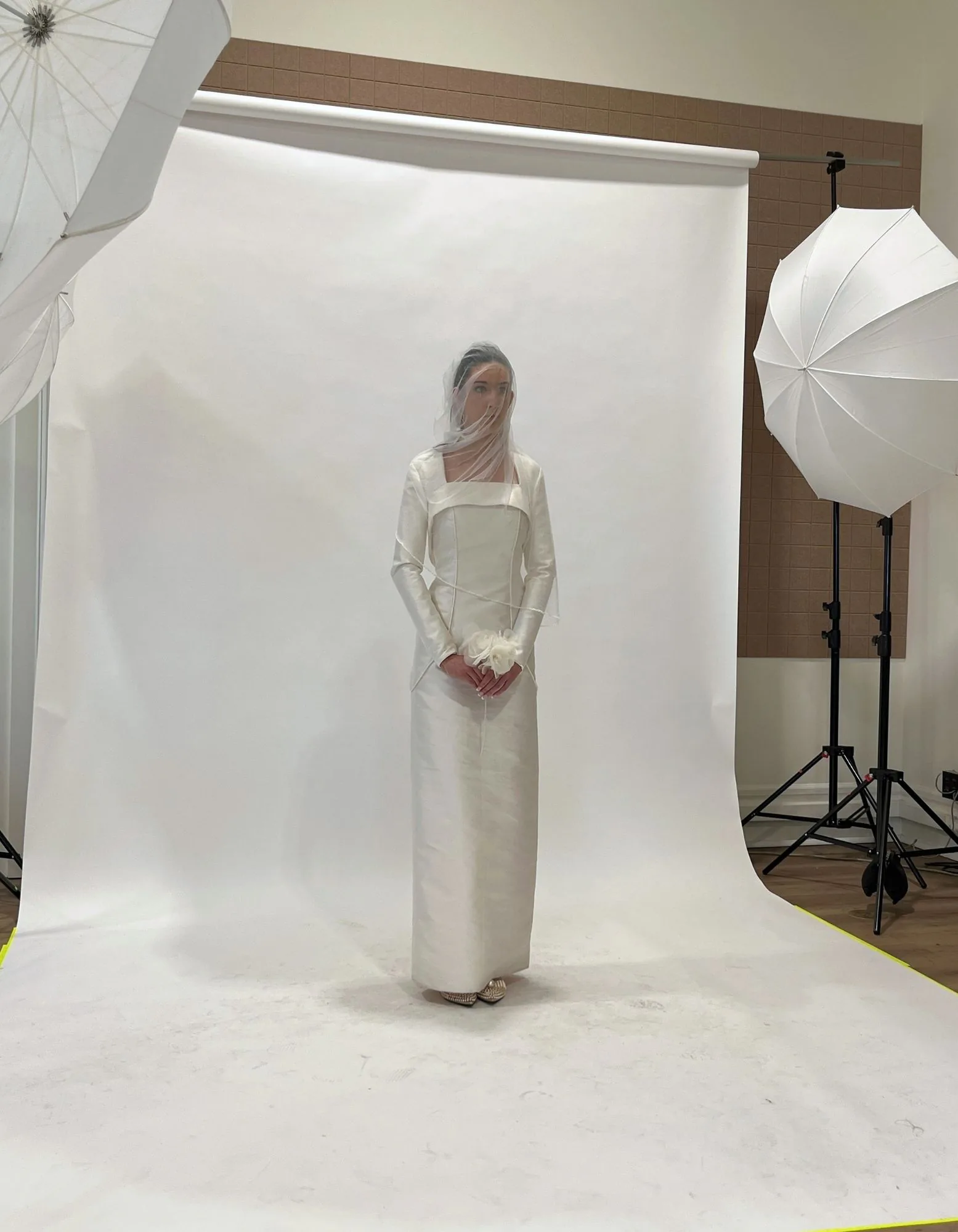 A veiled bridal look photographed in studio between white umbrellas and a paper backdrop.