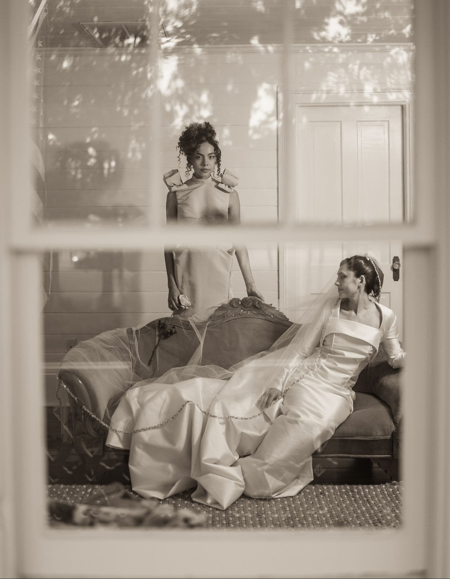 A sepia parlor portrait of the bride seated with the blush gown standing behind.