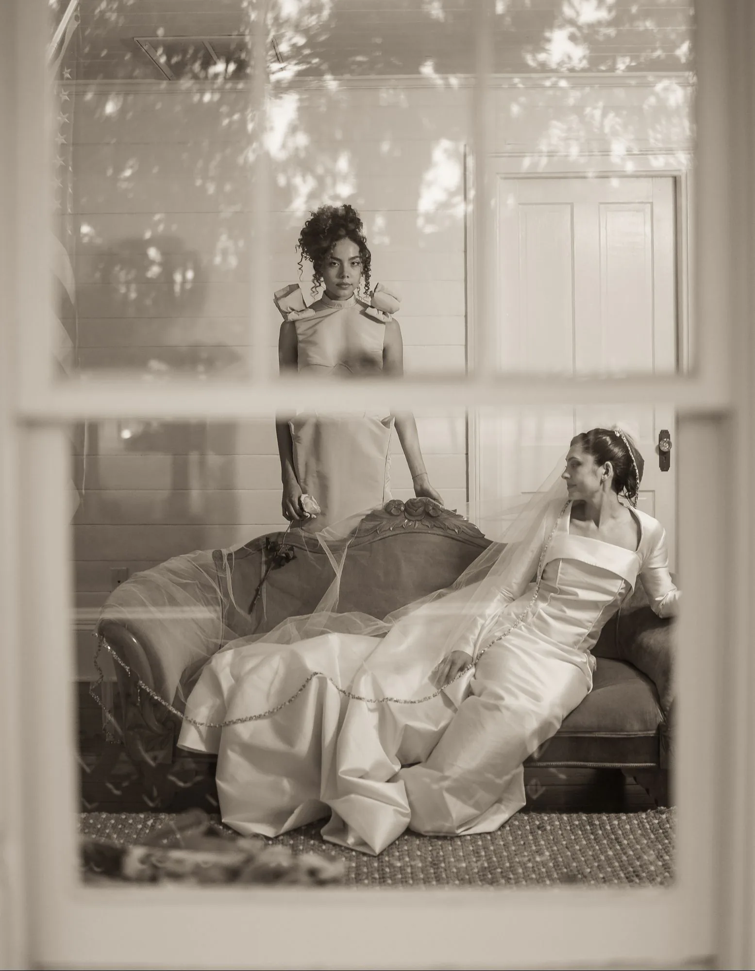 A sepia parlor portrait of the bride seated with the blush gown standing behind.