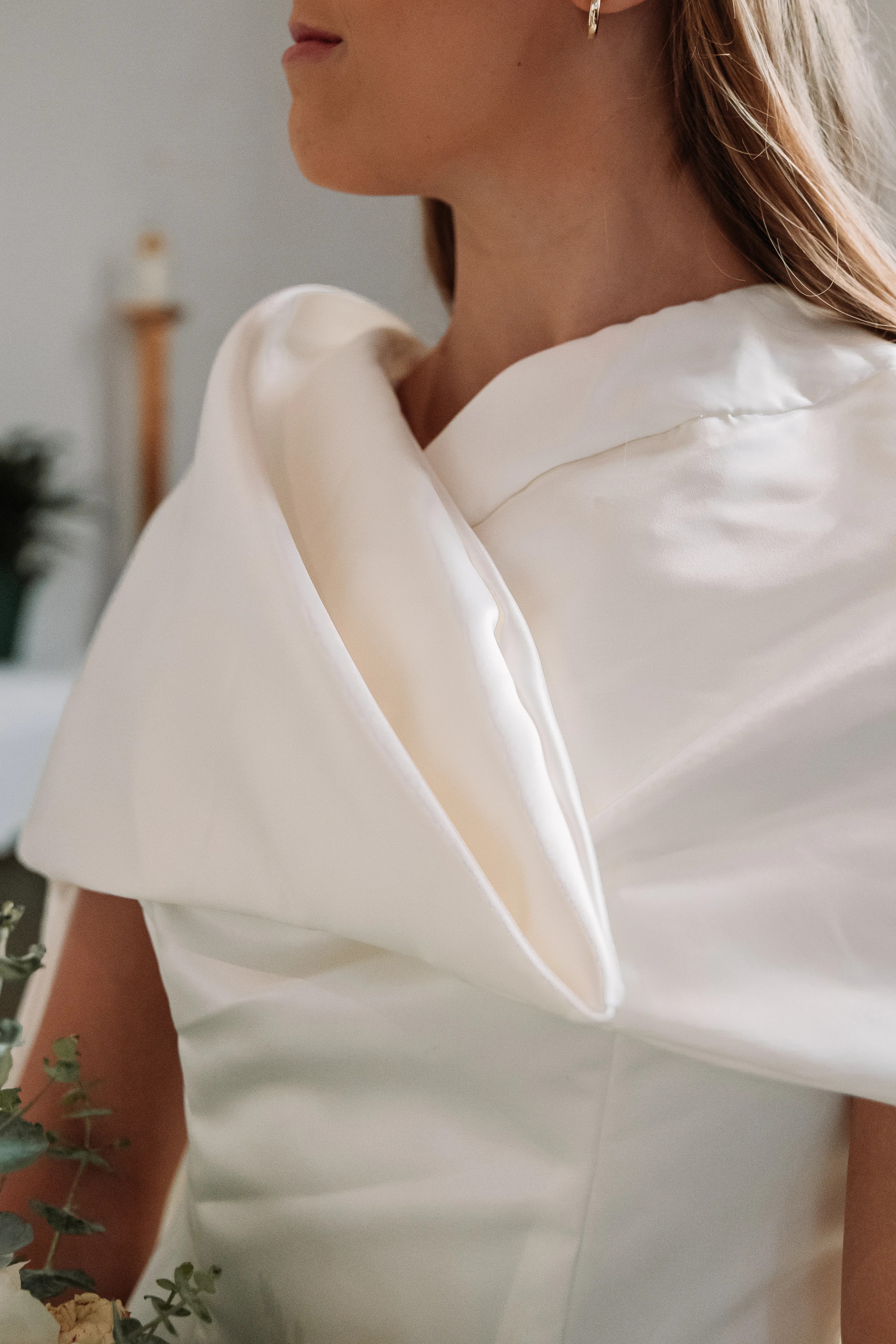 A close detail of the asymmetrical wedding dress neckline and sculpted satin shoulder.
