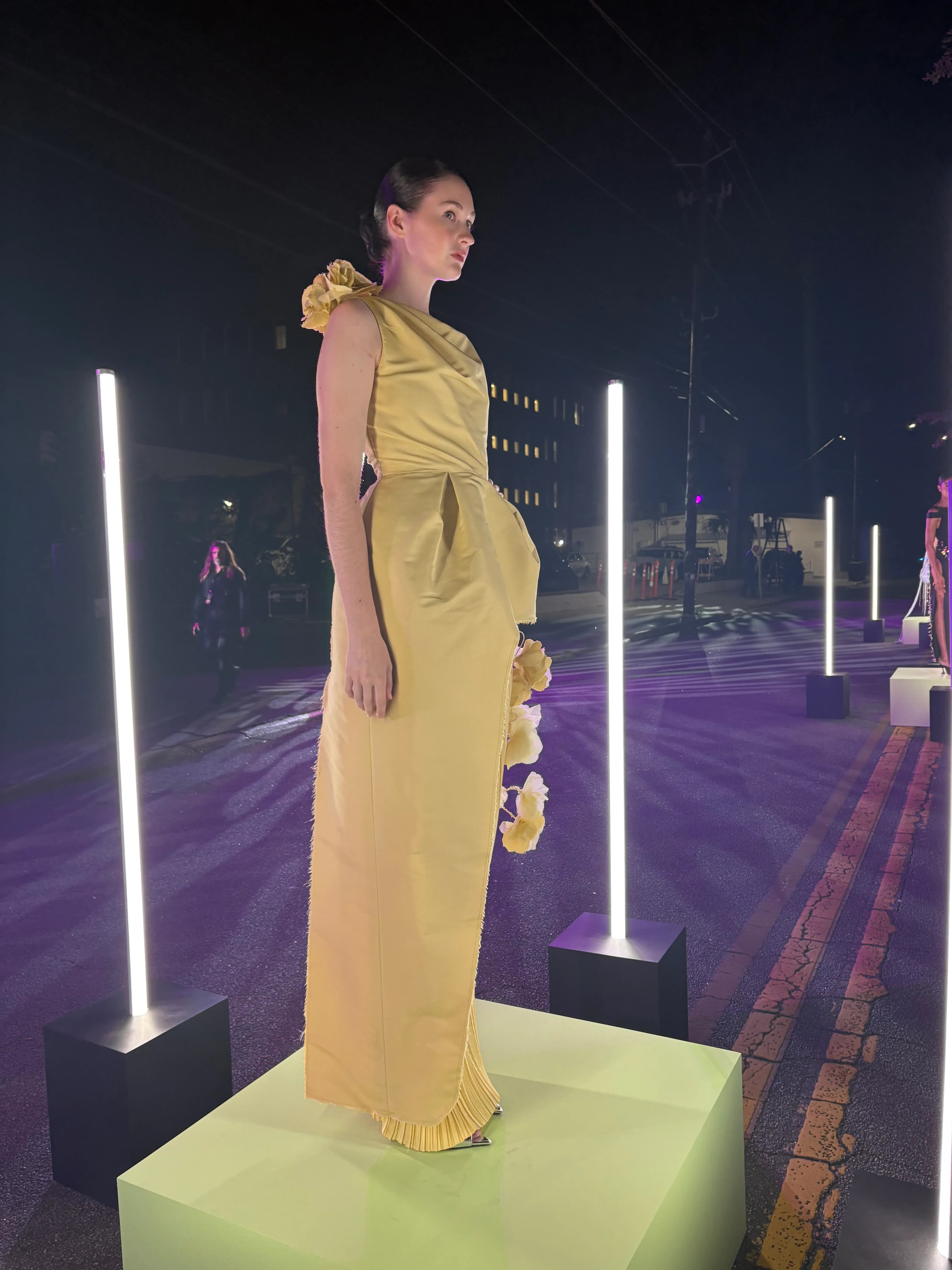 A side-profile evening installation portrait of the yellow Lanvin-inspired look displayed between glowing light columns.