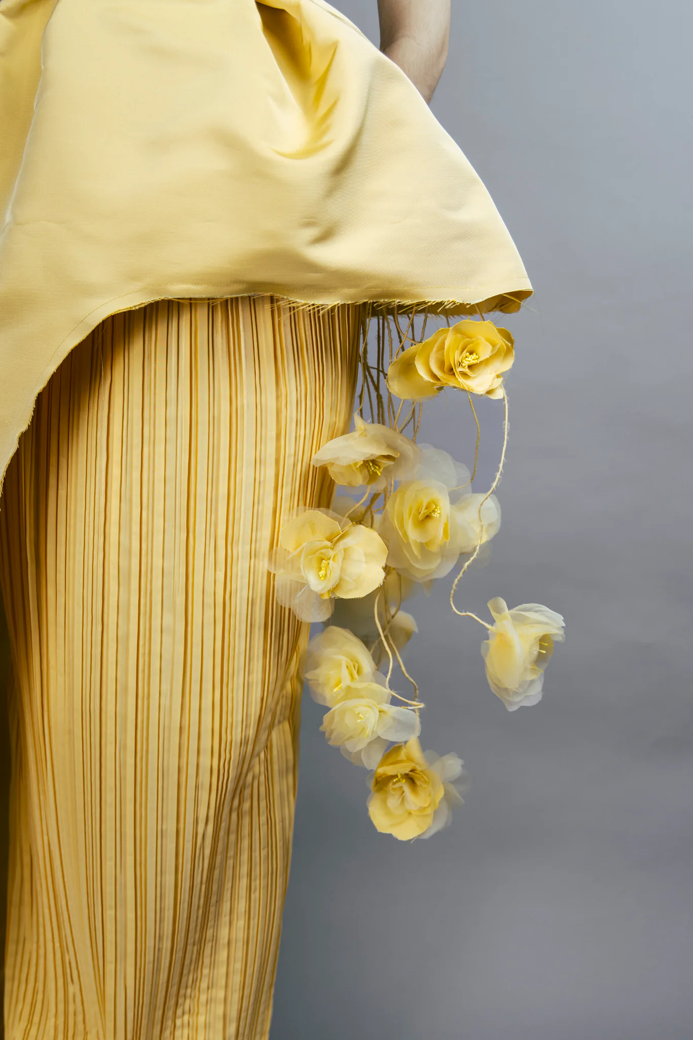A close detail of the pleated yellow skirt and suspended handmade flowers beneath the sculpted overskirt.