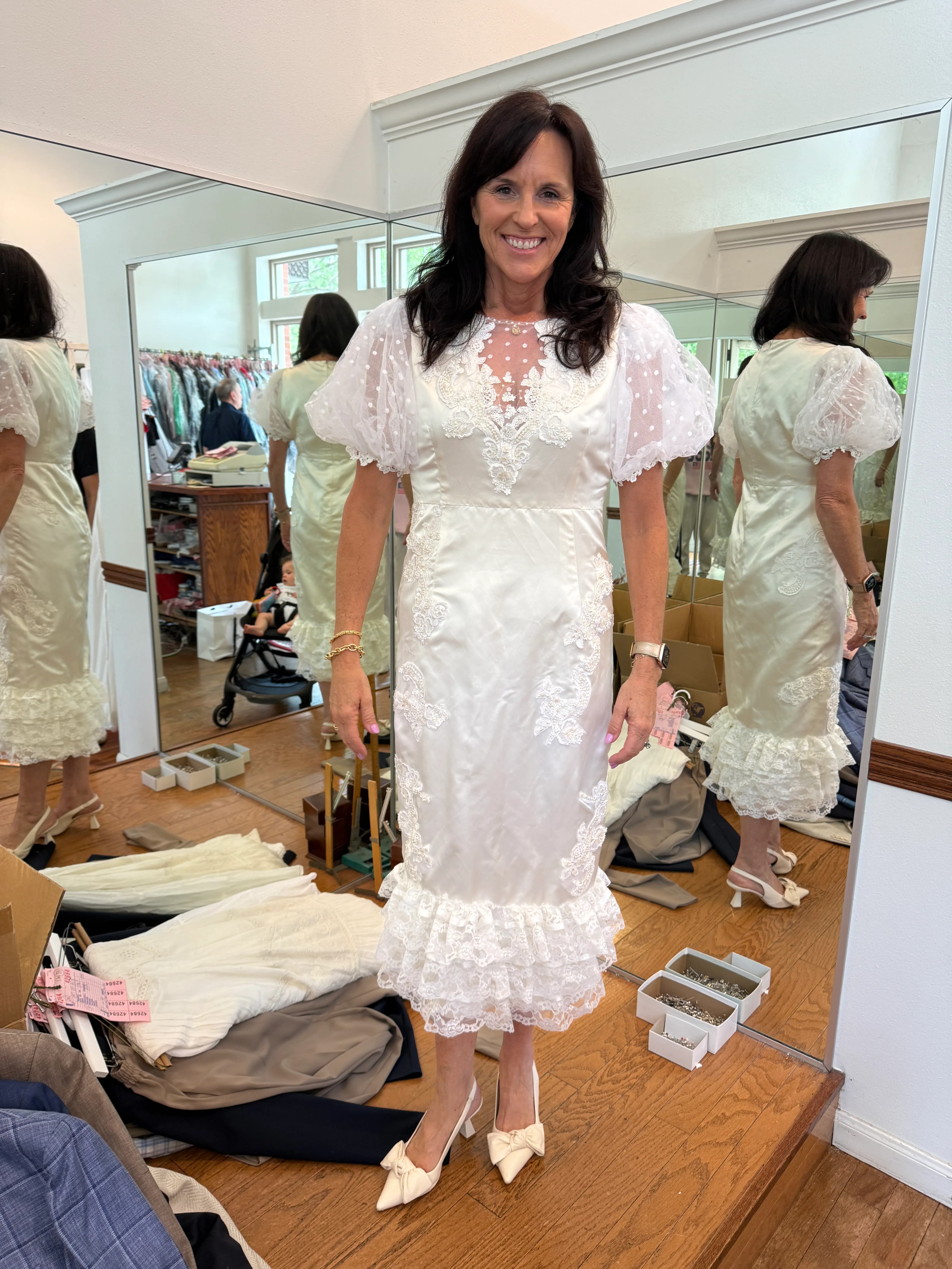 Samantha Covey's mother smiling during a fitting for the redesigned wedding dress, surrounded by studio mirrors.
