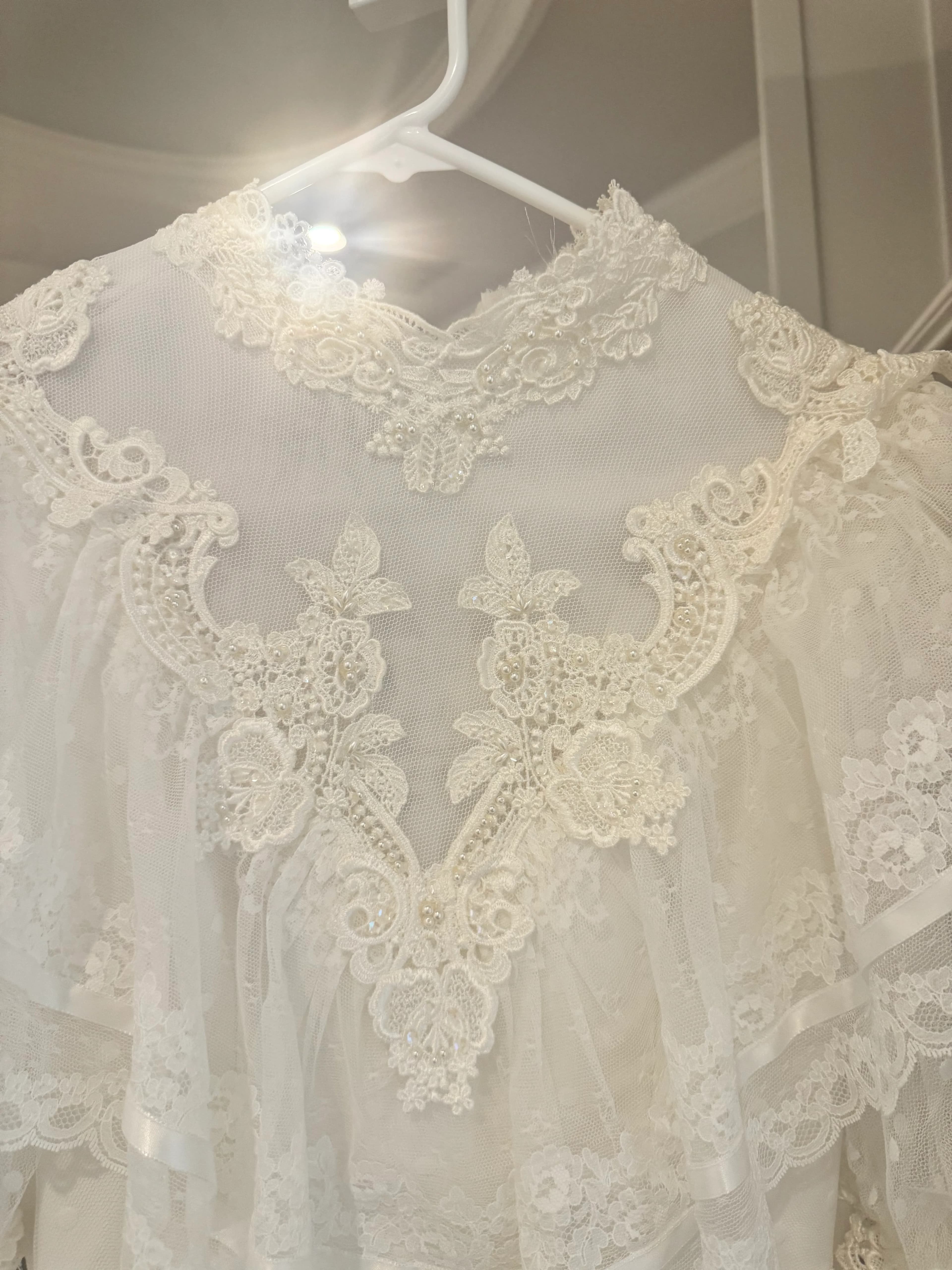 A process detail of the lace bodice and sheer neckline on a hanger.