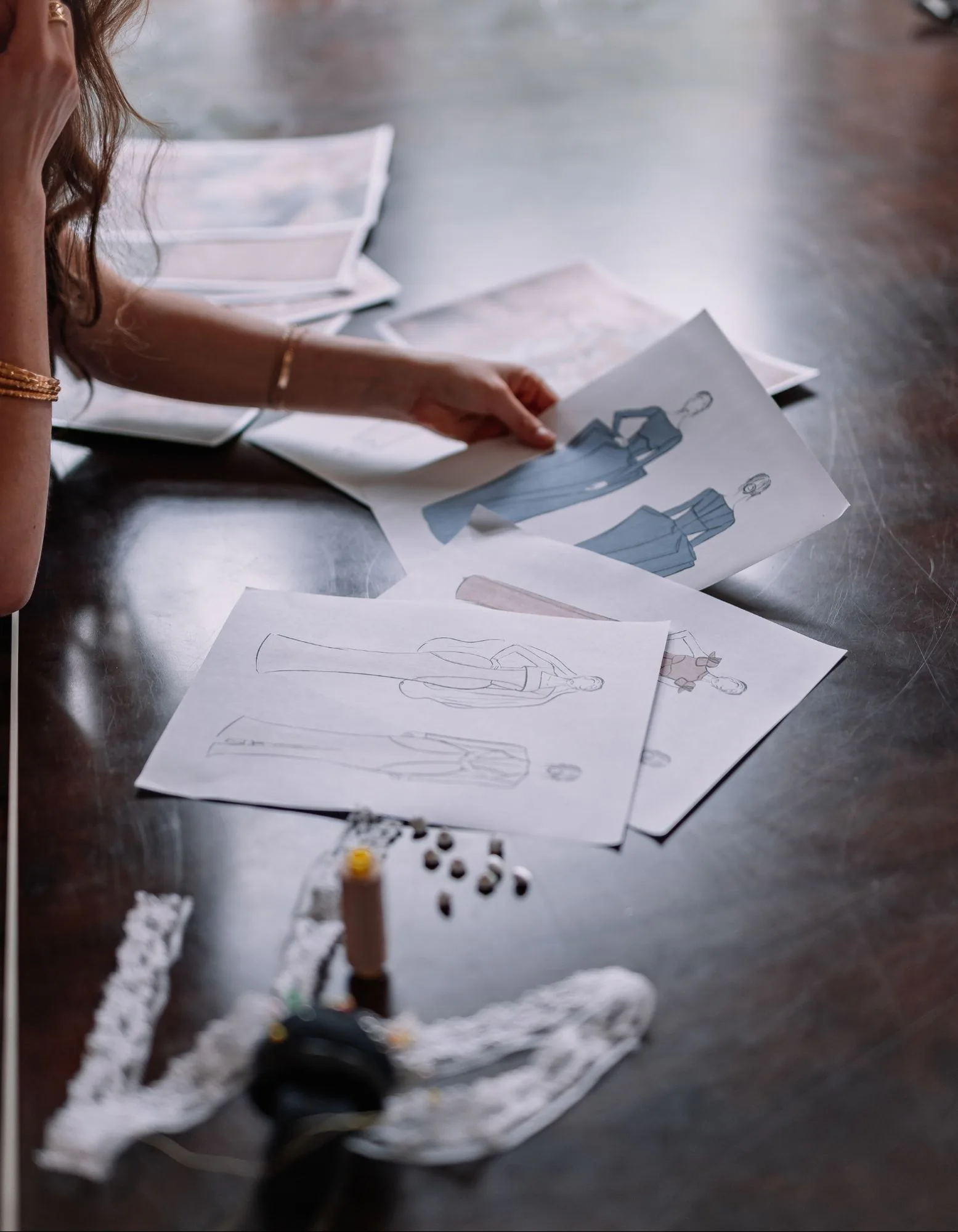 Samantha Covey reviewing blue formalwear sketches on an atelier worktable.