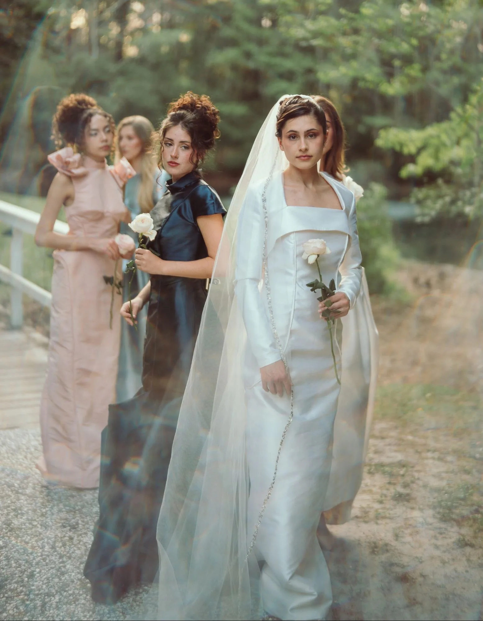 A veiled bride leading a formal procession across a white garden bridge.